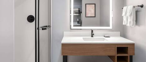 A modern bathroom with a glass shower enclosure, a white sink with a wooden vanity, and a large mirror.