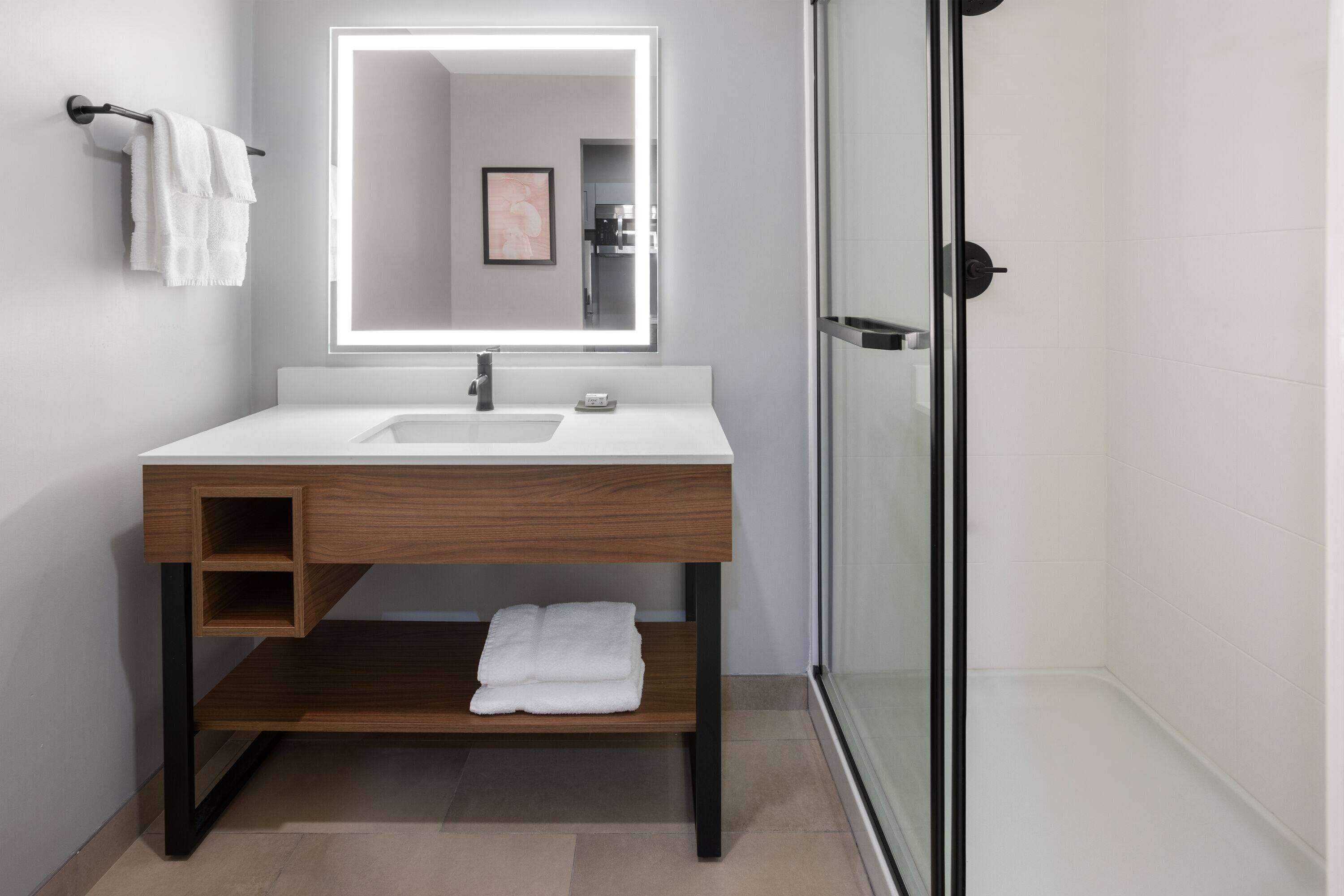 A modern bathroom with a wooden vanity, a large mirror, and a glass shower enclosure.