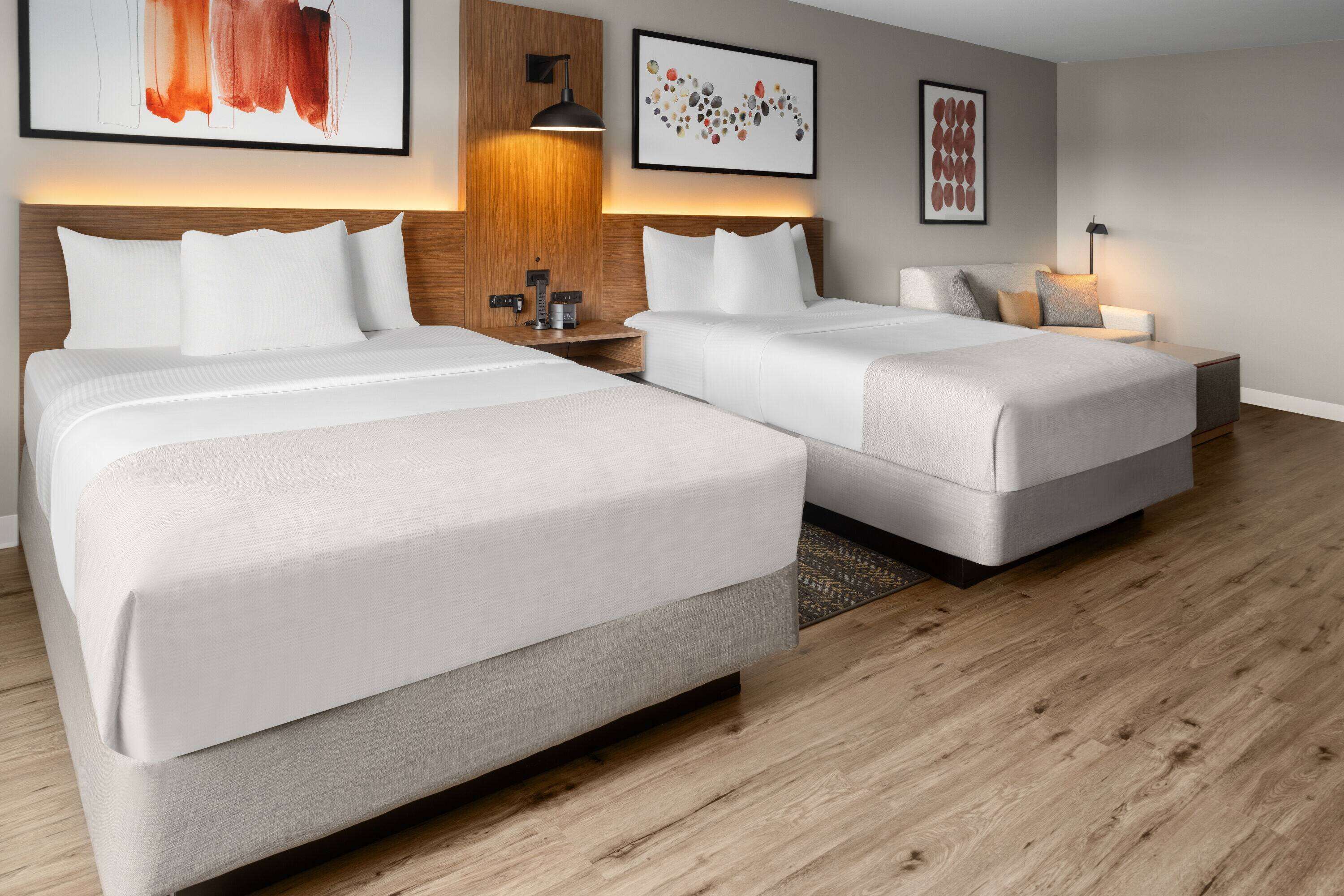 A hotel room with two beds, wooden headboards, and modern wall art.