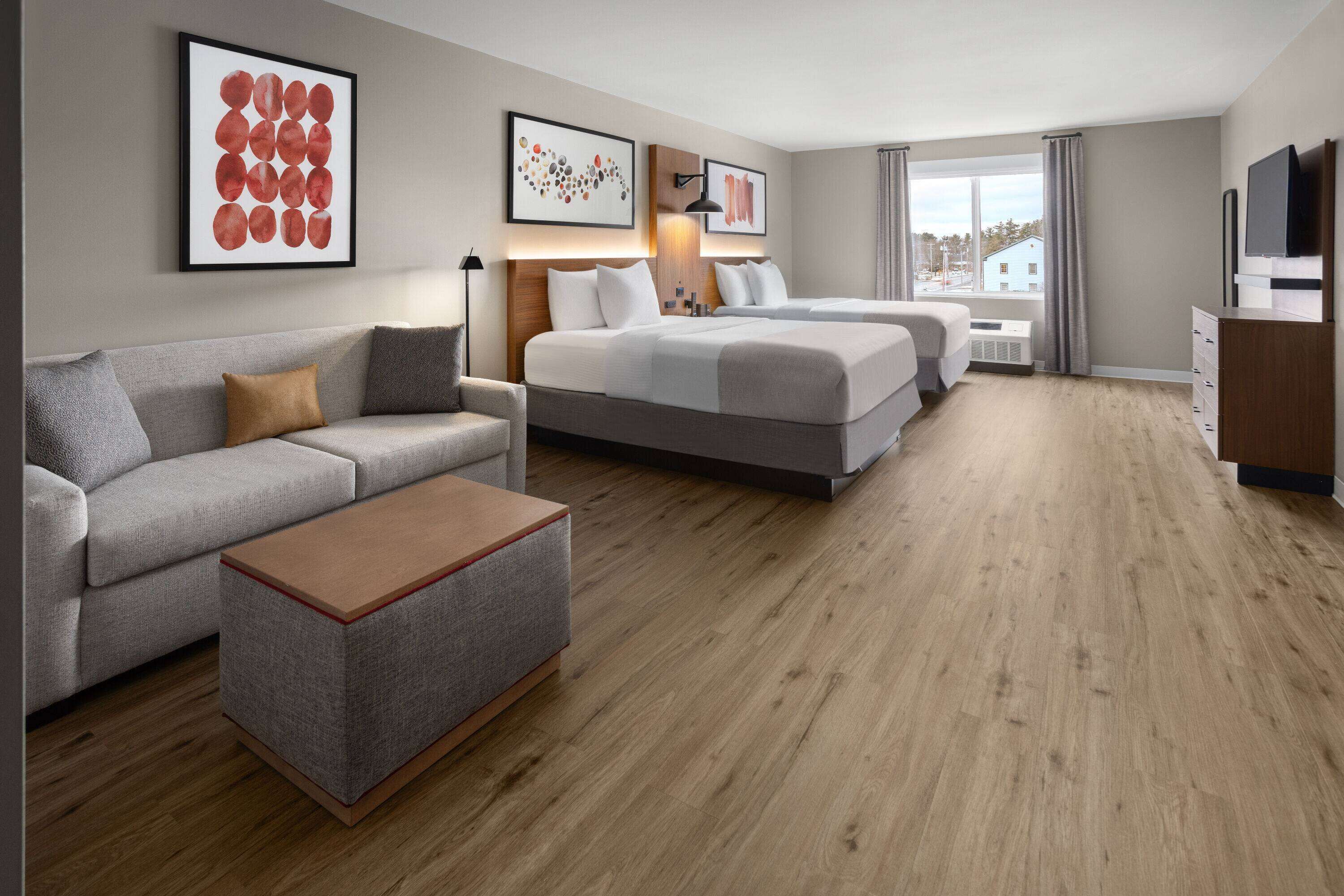 A modern hotel room with a sofa, a bed, a TV, and artwork on the walls.