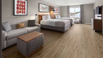 A modern hotel room with a sofa, a bed, a TV, and artwork on the walls.