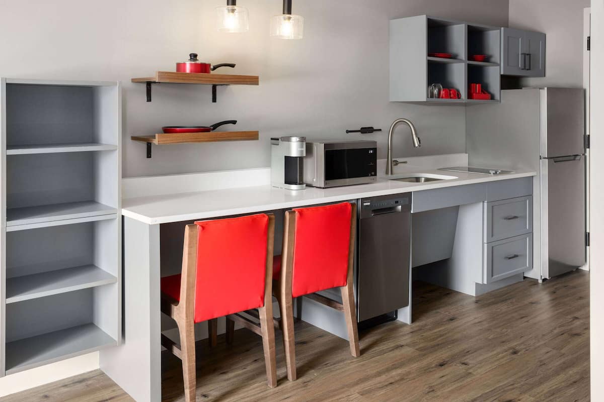 Une cuisine moderne avec des meubles blancs, un réfrigérateur en acier inoxydable, un four à micro-ondes, une machine à café et des chaises rouges.