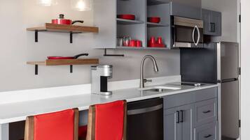 A modern kitchen with grey cabinets, a stainless steel refrigerator, a microwave, and red accents on shelves and chairs.
