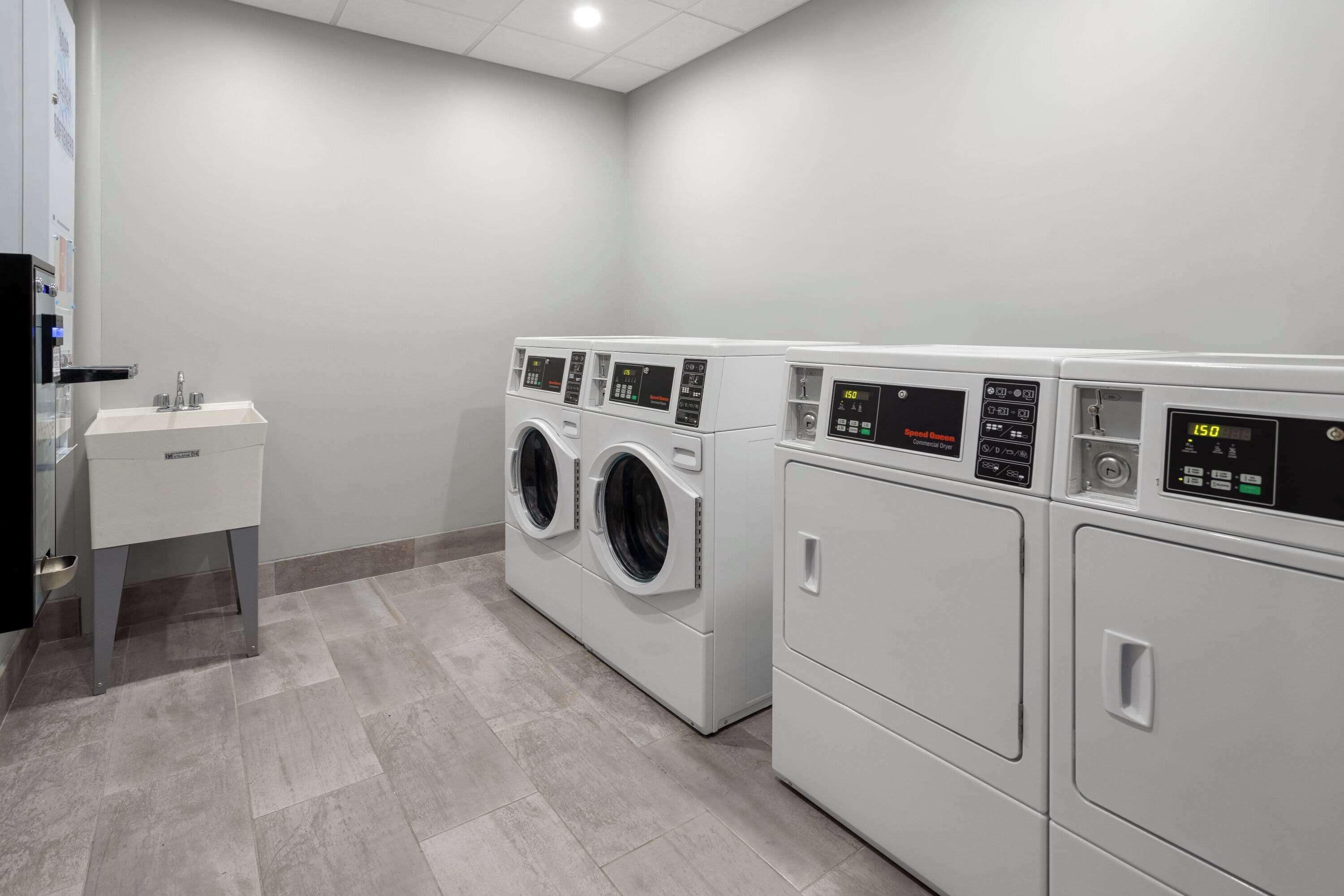 Een wasserette met drie wasmachines voor, een spoelbak en een klein kastje.