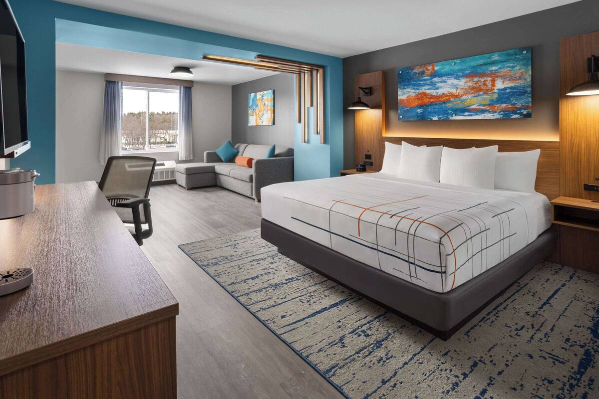 A modern hotel room with a large bed, a desk, a sofa, and a painting on the wall.