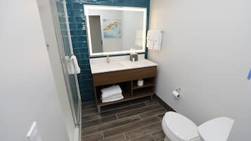 Un baño moderno con cabina de ducha de vidrio, un lavamanos blanco, un espejo grande con iluminación integrada y un inodoro.