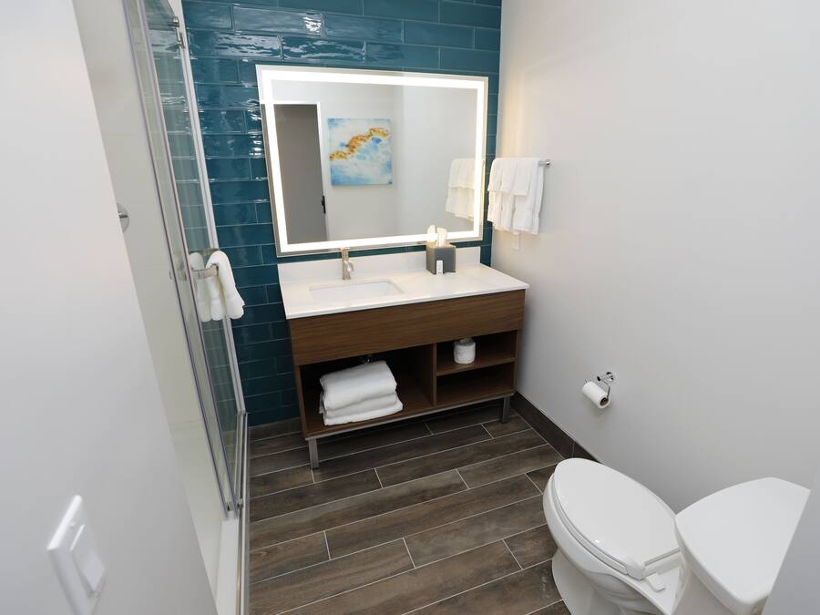 Een moderne badkamer met een douchecabine van glas, een witte wastafel, een grote spiegel met ingebouwde verlichting, en een toilet.