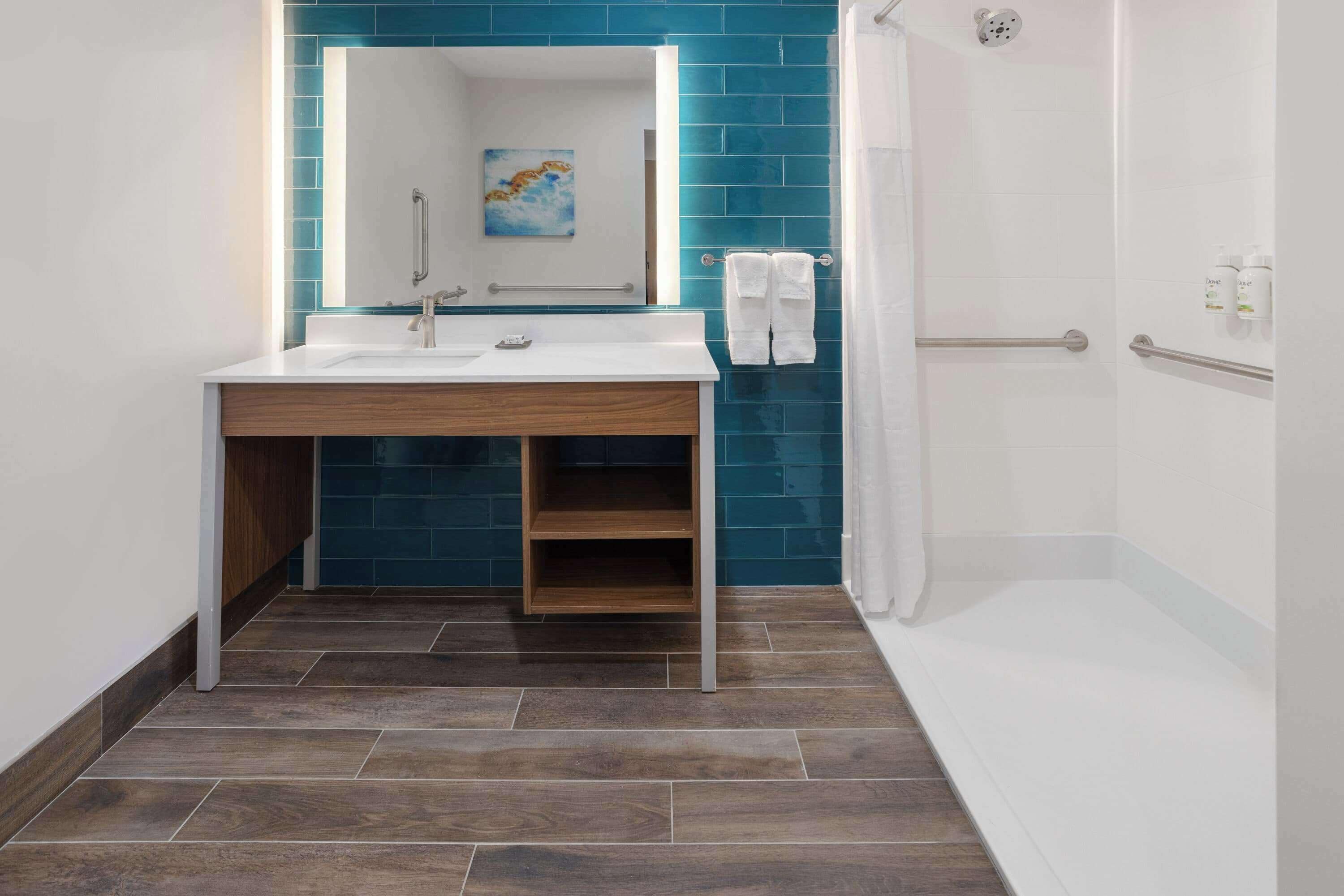 Un baño moderno con lavamanos blanco, paredes con azulejos azules, tocador de madera y cabina de ducha.