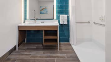 Un baño moderno con lavamanos blanco, paredes con azulejos azules, tocador de madera y cabina de ducha.