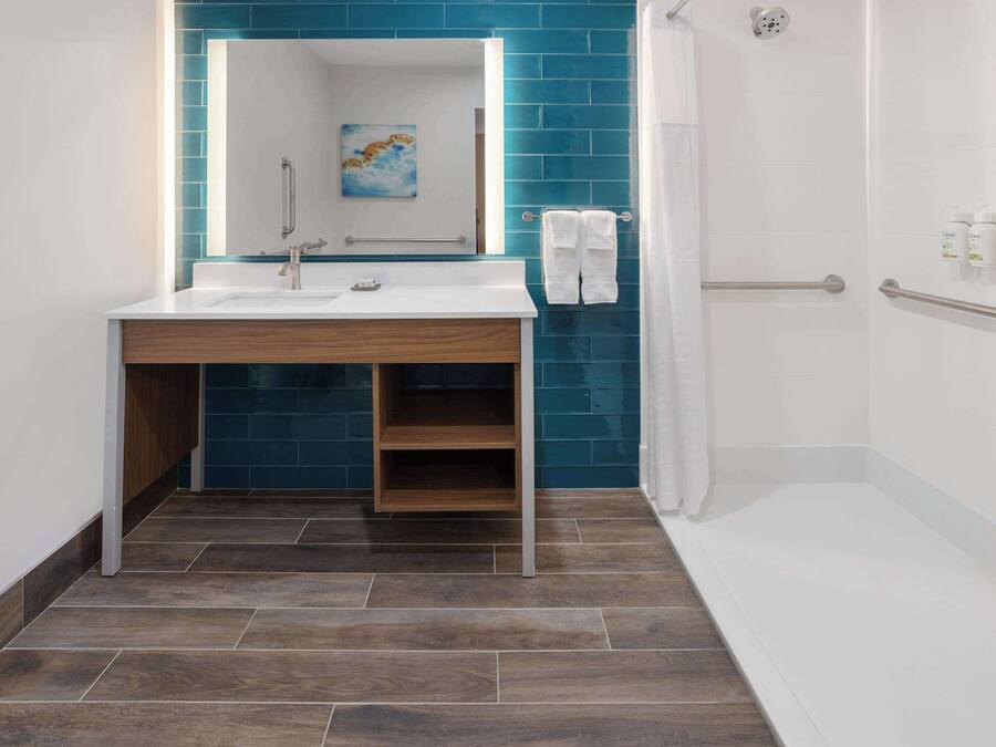 Un baño moderno con lavamanos blanco, paredes con azulejos azules, tocador de madera y cabina de ducha.