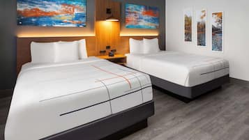 A hotel room with two beds, a wooden headboard, a nightstand, and three abstract paintings on the wall.