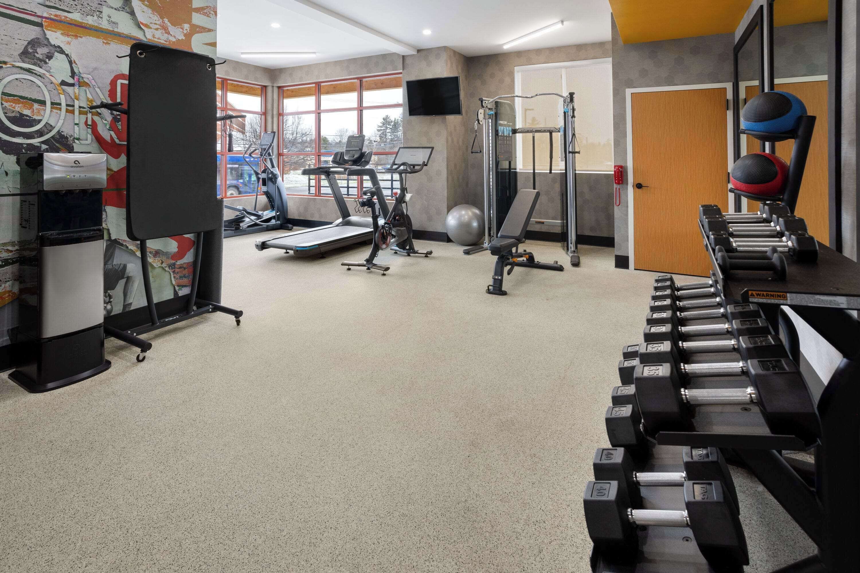 Un gimnasio con cintas de correr, máquinas de pesas y una variedad de mancuernas.