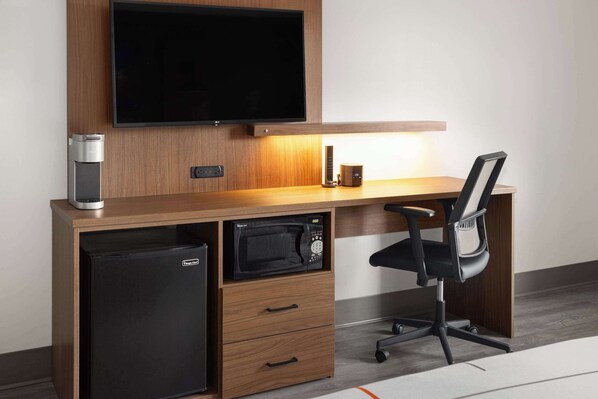 A compact office space with a built-in TV, a coffee machine, a microwave, and a black office chair. - La Quinta Inn & Suites By Wyndham Williston/Burlington (Williston)