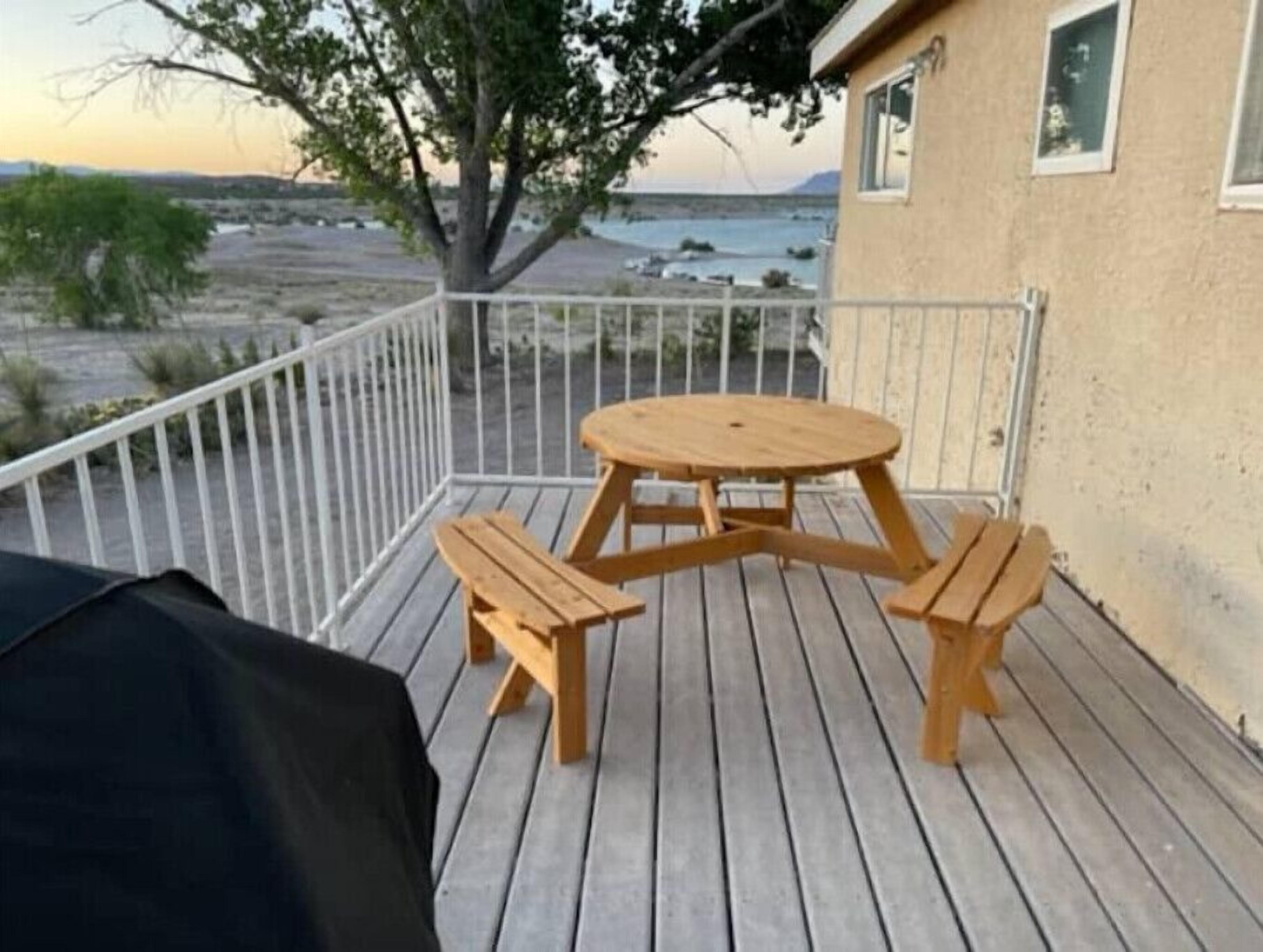 Eine Holzterrasse mit einem runden Tisch und Bänken, mit Blick auf Strand und Meer.