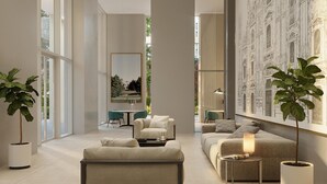 Un salon moderne avec un canapé, des fauteuils et une table basse. De grandes fenêtres offrent une vue sur un bâtiment à l’extérieur.