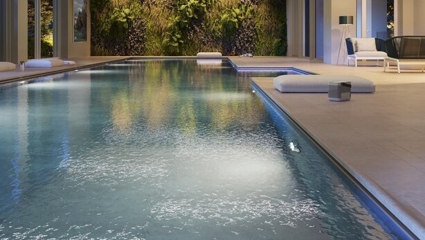 Une piscine intérieure moderne avec un mur de verre, un mur végétal et un espace détente comprenant un fauteuil et une lampe.