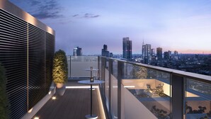Une terrasse moderne sur le toit, offrant une vue sur la ville, avec une balustrade en verre, une petite table ronde et des plantes en pot.
