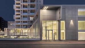 Un immeuble moderne de grande hauteur, doté d’une façade en verre et d’un espace commercial au rez-de-chaussée, sur lequel on peut lire l’inscription « Torre Milano ».