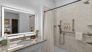 A bathroom with a large mirror, a sink, a shower with a handheld showerhead, and two bottles of shampoo. - Little Inn on Main 214 West Main Street (Washington)