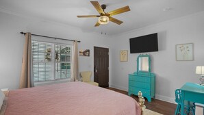 A bedroom with a bed, a ceiling fan, a dresser, a chair, and a TV on the wall.