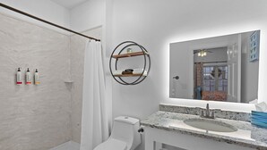 A modern bathroom with a shower, toilet, and sink. There are three bottles on the floor, a towel rack with a towel, and a mirror above the sink. - Little Inn on Main 214 West Main Street (Washington)