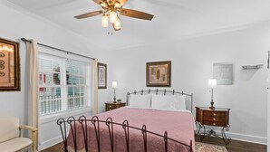 A bedroom with a bed, a ceiling fan, a window with blinds, a nightstand, a chair, and a rug.
