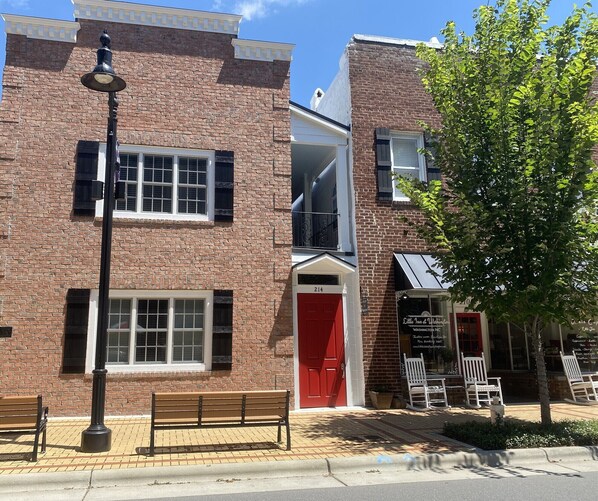 A brick building with a red door, a bench, and a street lamp.