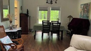 A spacious living room with a dining area, wooden flooring, a chandelier, and a large window with a view of greenery. - Become at peace in a comfortable country home (New Paltz)