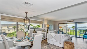 A spacious living room with a dining area, large windows, and a balcony with a view of the neighborhood. - Your Family Friendly Vacation Awaits! Olympic Size Pool! Short Walk to Beach (Pensacola Beach)