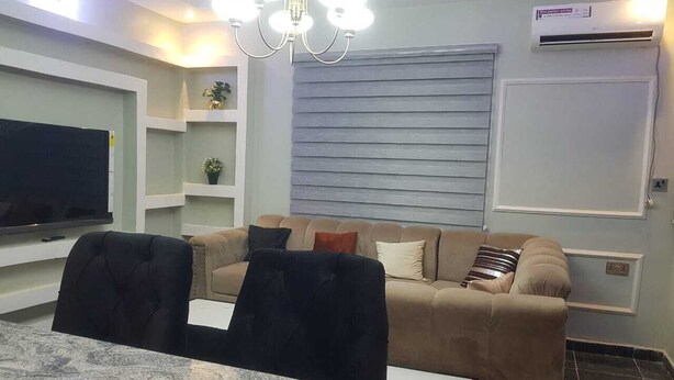 A modern living room with a sofa, a dining table with chairs, a flat-screen TV, and a chandelier. - Enjoy this unique, lavishly furnished 1-bed apartment with "Open Kitchen Design" (Lagos)