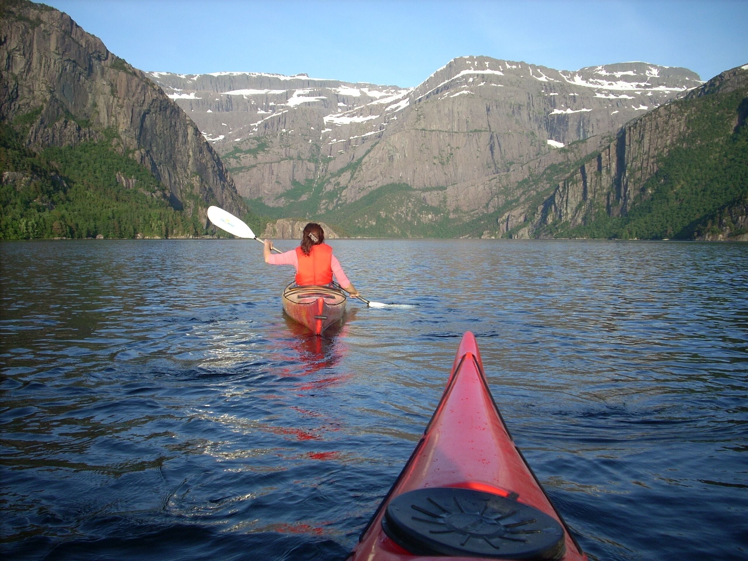 Una persona haciendo kayak en un lago tranquilo con montañas al fondo.