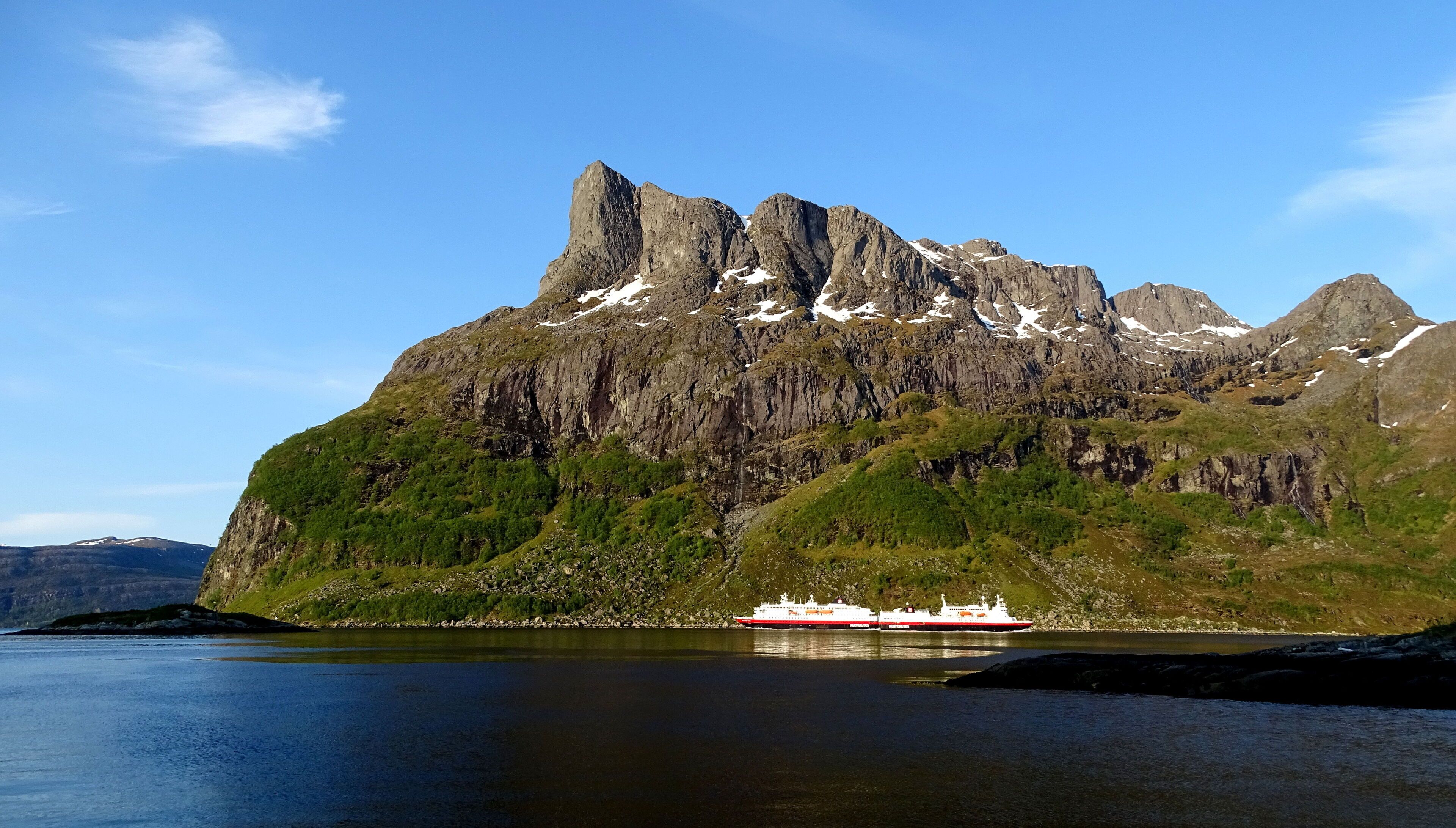 A cruise ship docked at a fjord with a mountain backdrop.