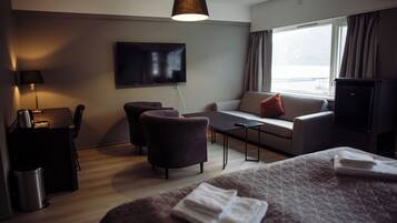 A modern hotel room with a bed, a sofa, a desk, a TV, and a window with curtains.