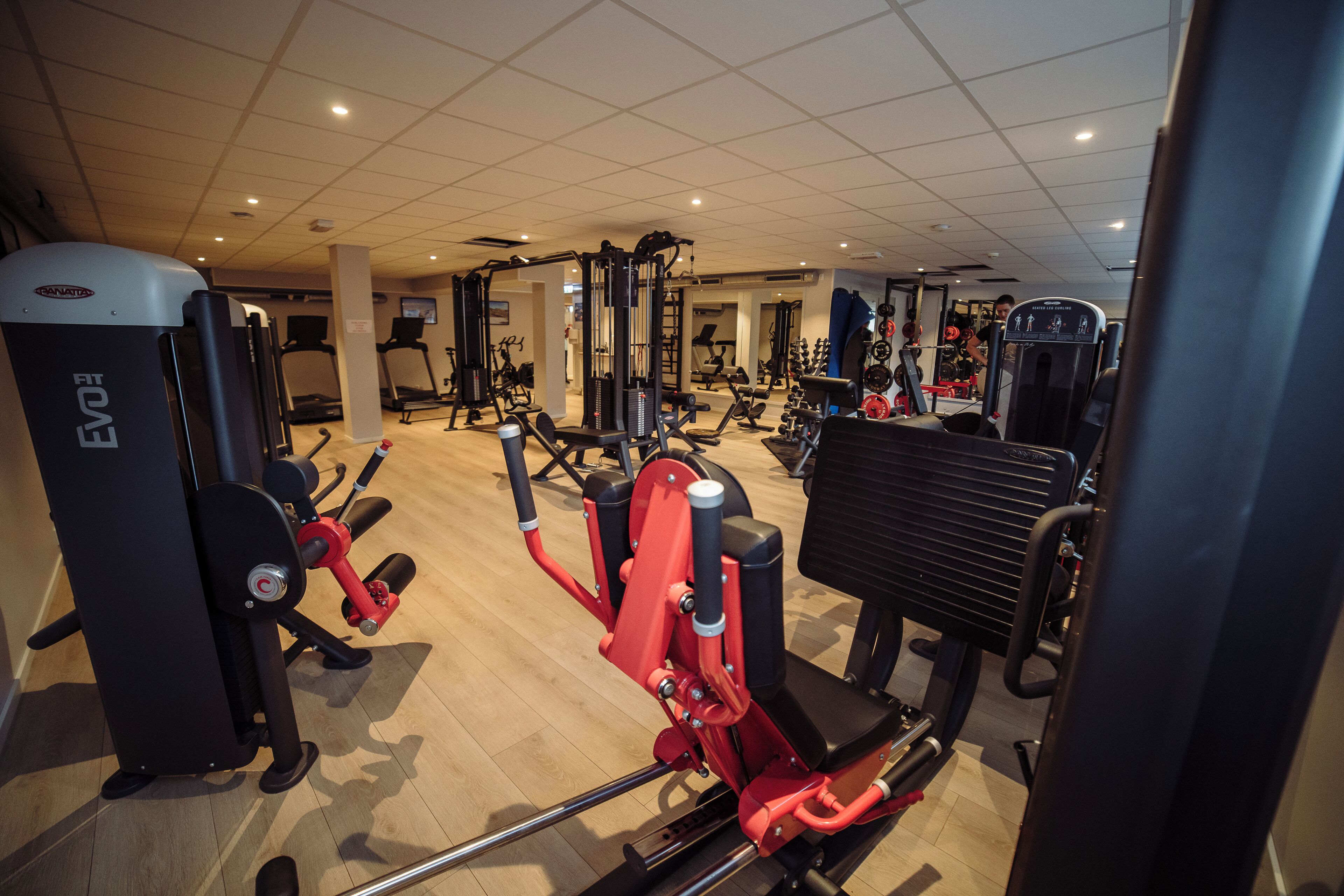 A gym with various exercise machines, including a red and black machine in the foreground.