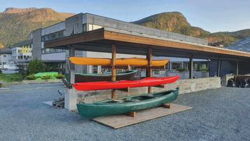 Una filera de kayak sobre una plataforma de fusta davant d'un edifici de disseny modern amb una muntanya de fons.