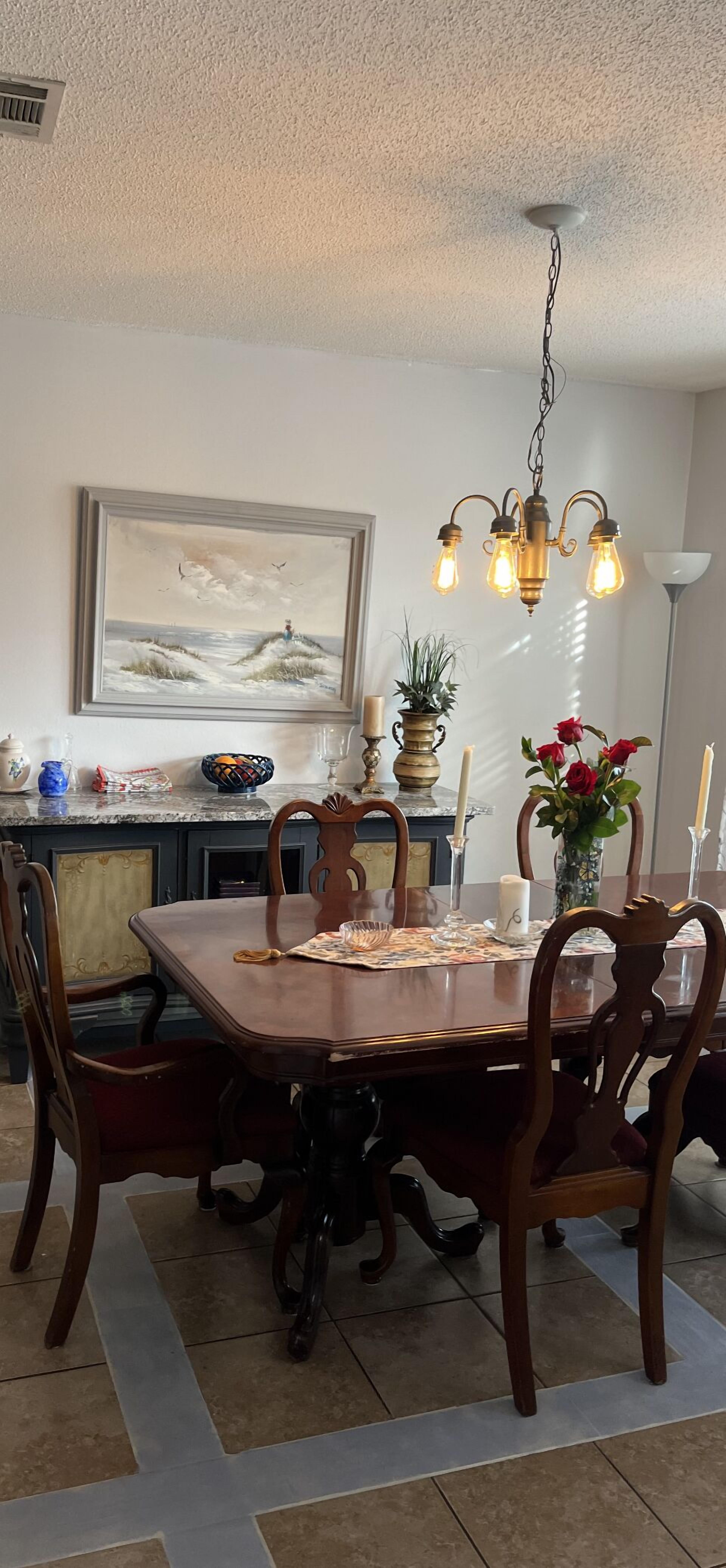 A dining area with a wooden table, chairs, a chandelier, and a painting on the wall.