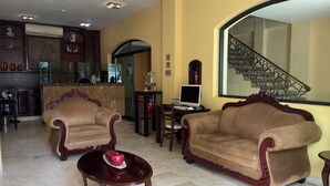 Un vestíbulo de hotel con dos sofás, una mesa de centro, un mostrador de recepción y una escalera.