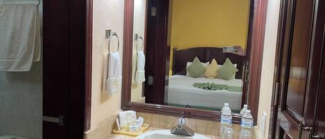 A bathroom with a sink, mirror, toiletries, and a towel rack.