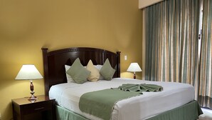 Una cama bien hecha con falda verde, dos lámparas de noche y un cabecero de madera.