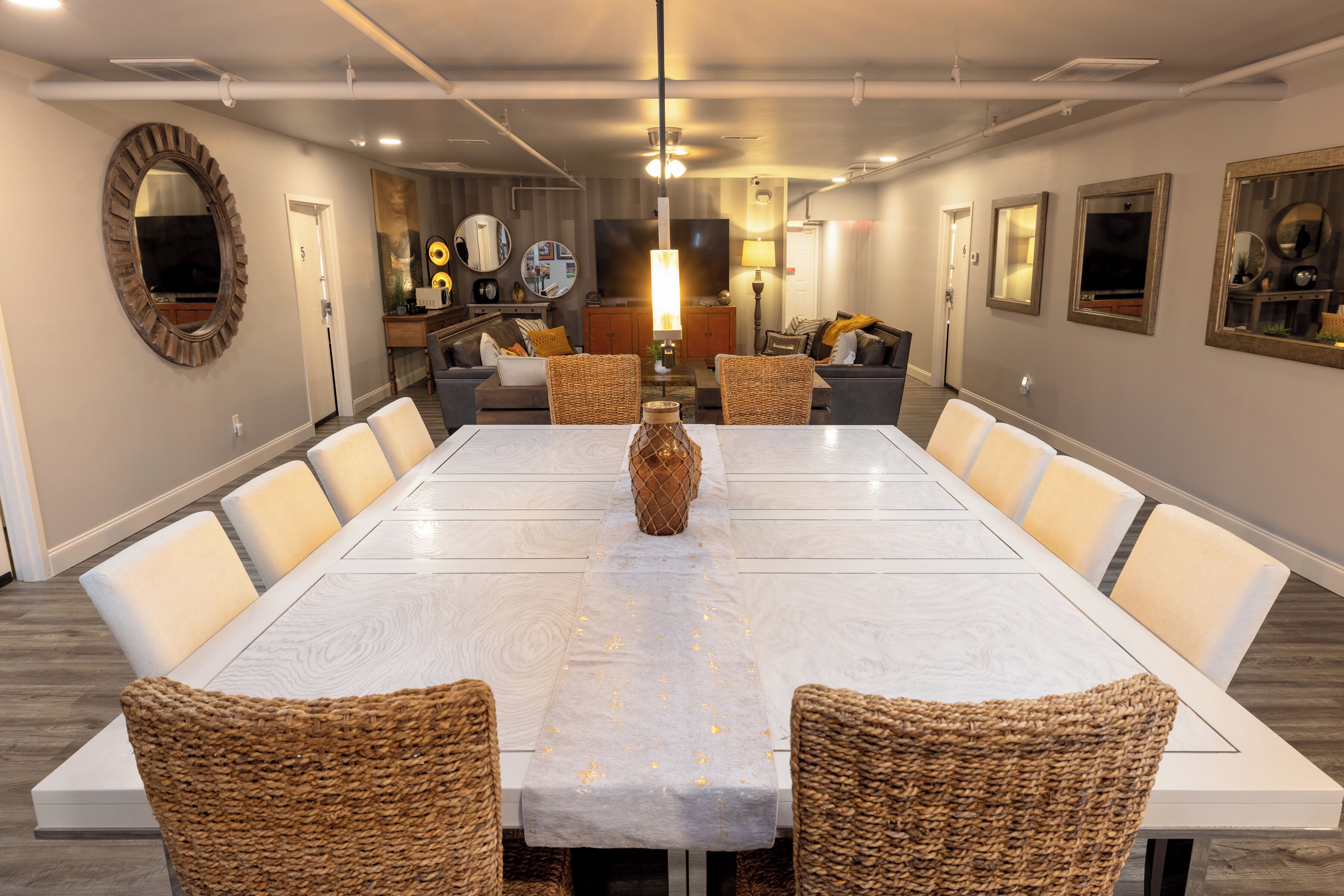 A spacious dining area with a long table, wicker chairs, and a central decorative vase.