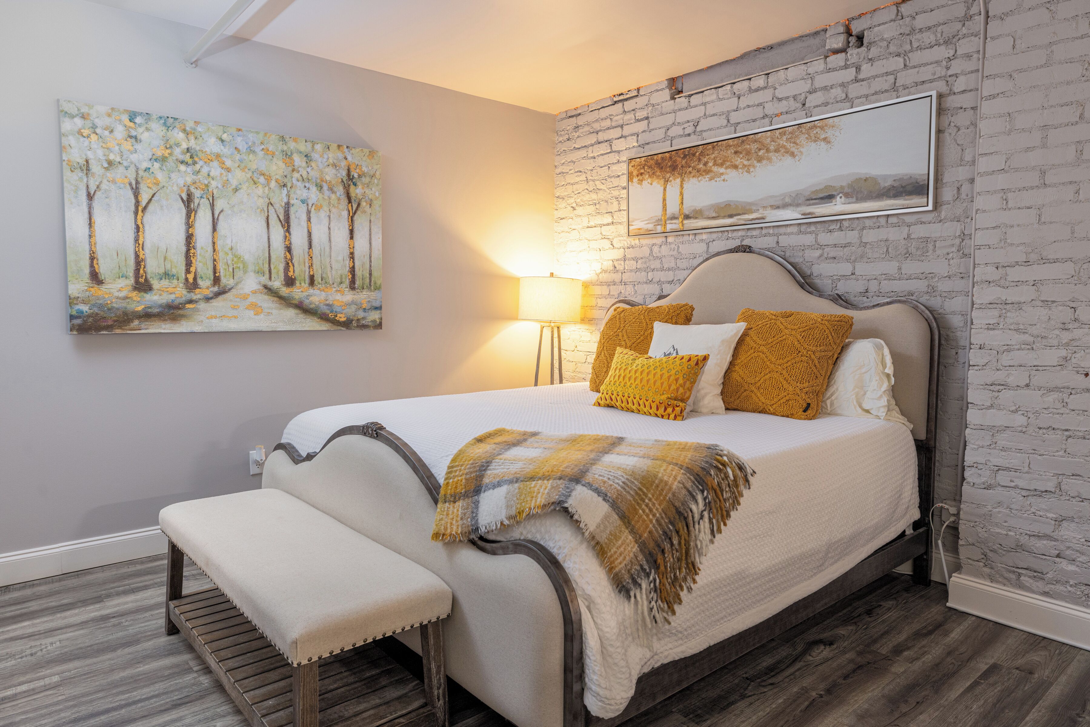 Un dormitorio con cama, banco y dos cuadros en la pared.