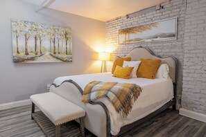 A bedroom with a bed, bench, and two paintings on the wall.