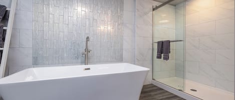 Un baño moderno con una bañera independiente, ducha con mampara de cristal y pared de azulejos.