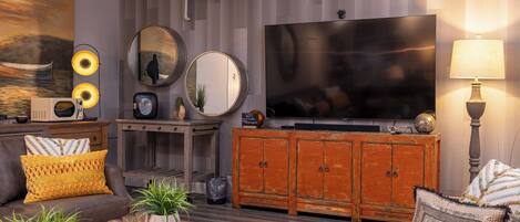 Un salon moderne doté d’un grand téléviseur à écran plat, d’un meuble en bois, d’un canapé agrémenté de coussins à motifs et d’une table basse ornée d’objets décoratifs.