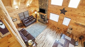 Interno di una baita con camino in pietra, pareti in legno, un divano in pelle e zona pranzo.