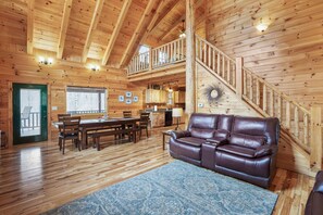 A wooden cabin interior with a dining area, a leather sofa, and a staircase.