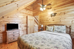 A cozy log cabin bedroom with a bed, dresser, television, and a ceiling fan. - Applewood Lodge | Hocking Hills, Hot Tub, Fire Pit (Logan)