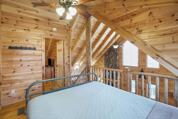 A wooden cabin interior with a bed, a ceiling fan, and a stone fireplace.