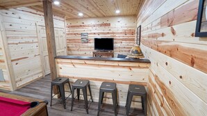 Un interno in legno con un'area bar, sgabelli, una televisione e un quadro appeso al muro.