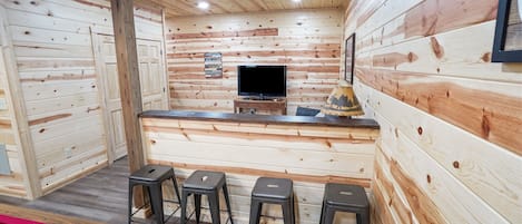 Un interior de madera con mesa de billar, taburetes de bar y televisión.